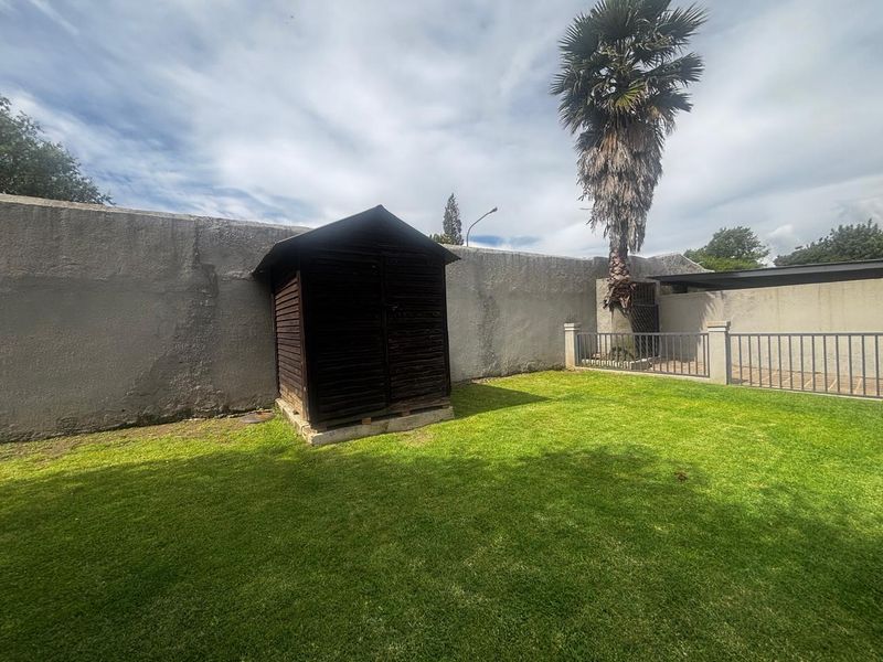 A private garden area featuring a lawn, a wooden storage shed, and a high perimeter wall providing enclosure.