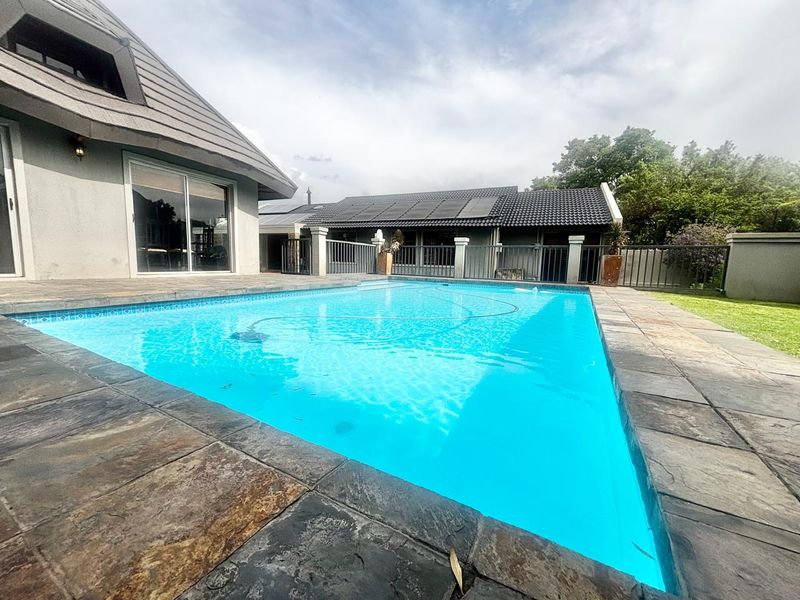 A well-maintained swimming pool area featuring stone coping, surrounded by a paved patio and adjacent to the main dwelling with solar panels.
