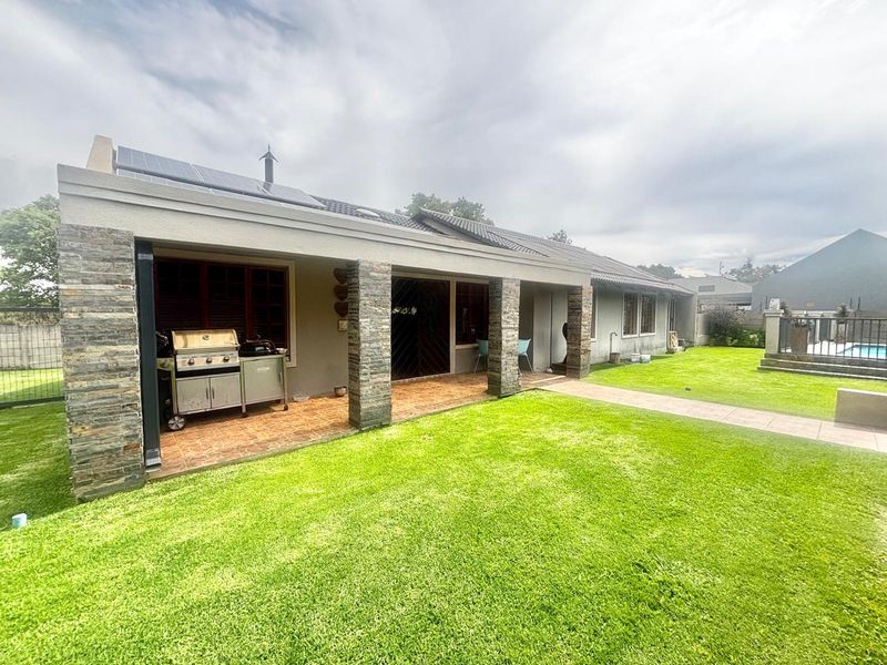 A covered patio area featuring stone-clad pillars and tiled flooring, overlooking a well-maintained lawn with solar panels installed on the roof.