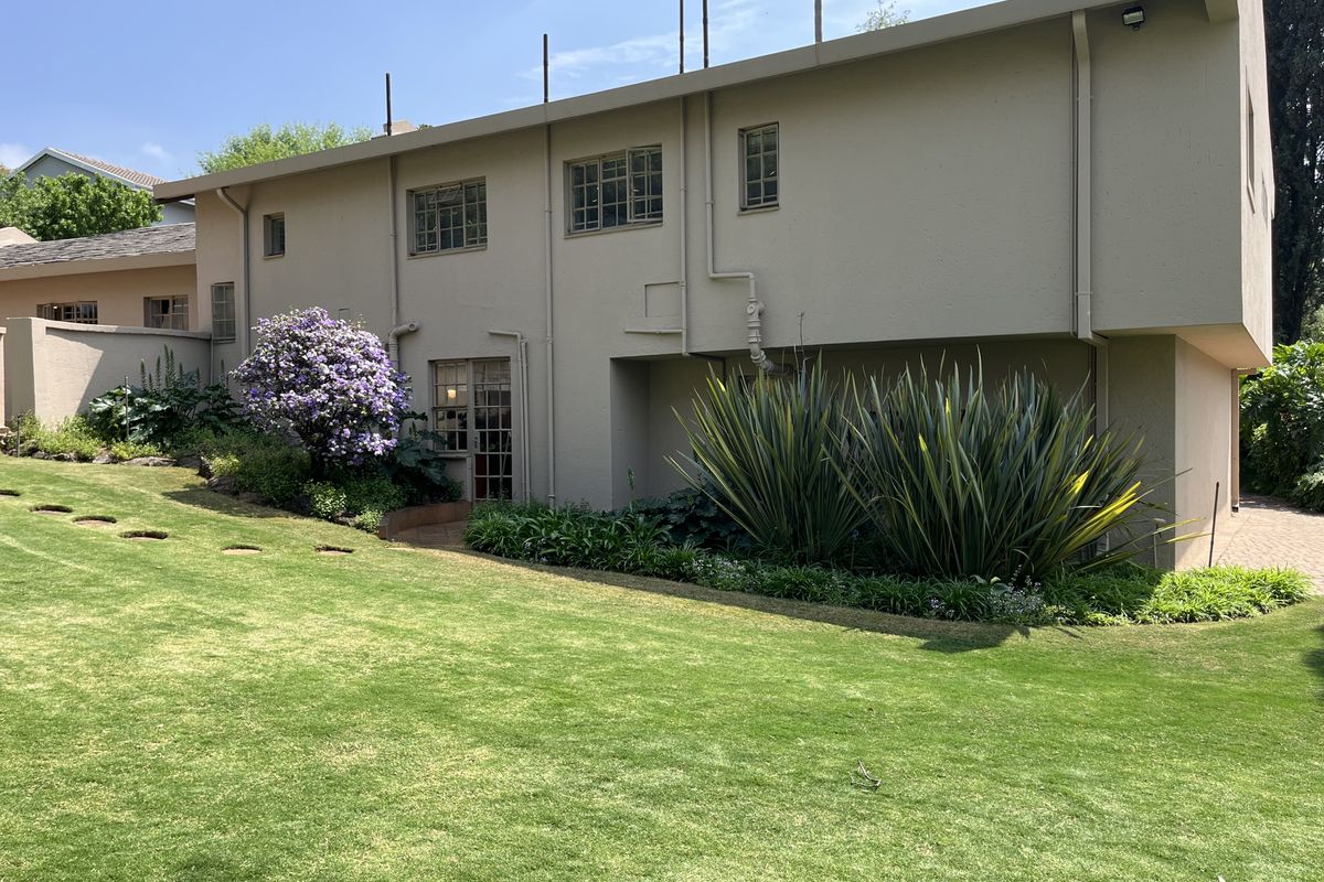 A view of the rear exterior elevation of the house, featuring a well-maintained lawn, landscaped garden beds, and established shrubbery.