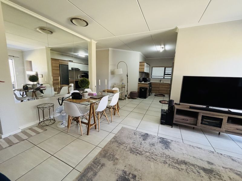 Open-plan living and dining area featuring tiled flooring, mirrored wall accents, and a connected kitchen space with modern cabinetry.