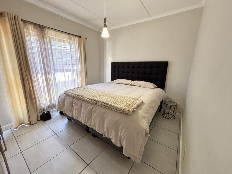 A well-lit bedroom featuring neutral tiled flooring, a sliding glass door providing natural light, and a modern pendant light fixture.