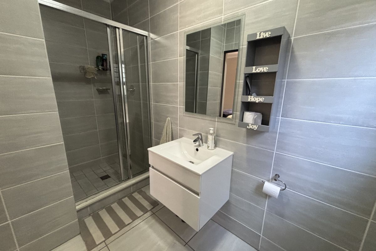 Modern bathroom featuring a glass shower enclosure, wall-mounted vanity with basin, and neutral grey wall and floor tiling.