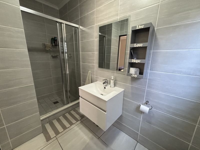 Modern bathroom featuring a glass shower enclosure, wall-mounted vanity with basin, and neutral grey wall and floor tiling.