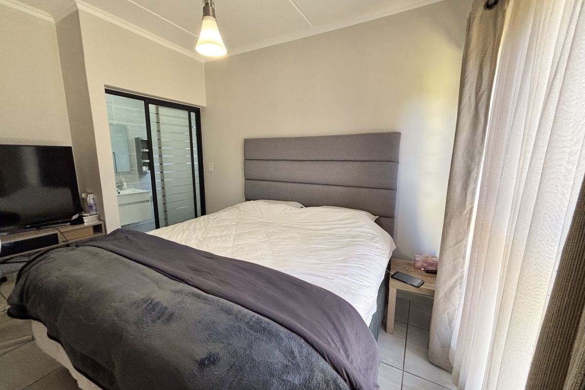 A well-maintained bedroom featuring tiled flooring, a modern pendant light, and a sliding glass door providing a view into the adjacent bathroom.