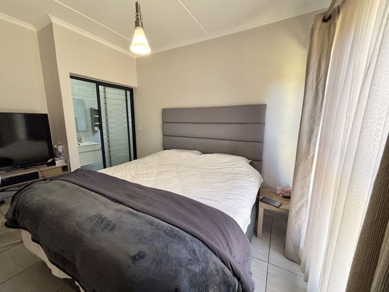 A well-maintained bedroom featuring tiled flooring, a modern pendant light, and a sliding glass door providing a view into the adjacent bathroom.