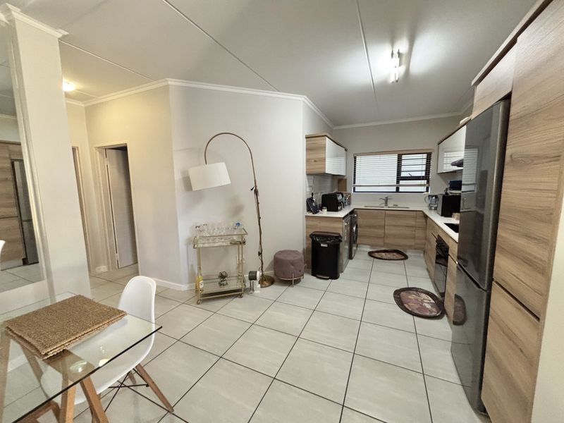 Open-plan kitchen and living area featuring modern wood-finish cabinetry, tiled flooring, and integrated appliances in a well-maintained apartment setting.