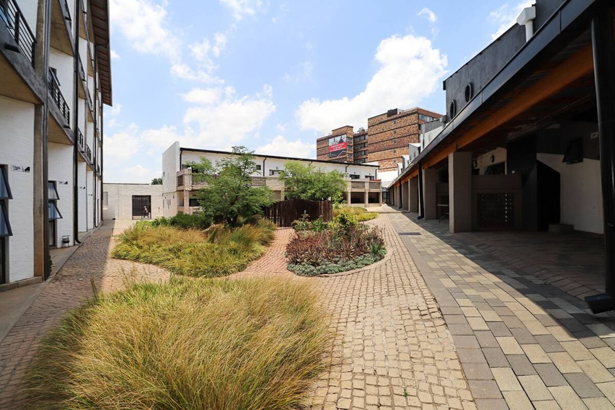 A well-maintained communal courtyard area featuring paved walkways, landscaped garden beds, and covered access paths between apartment building wings.
