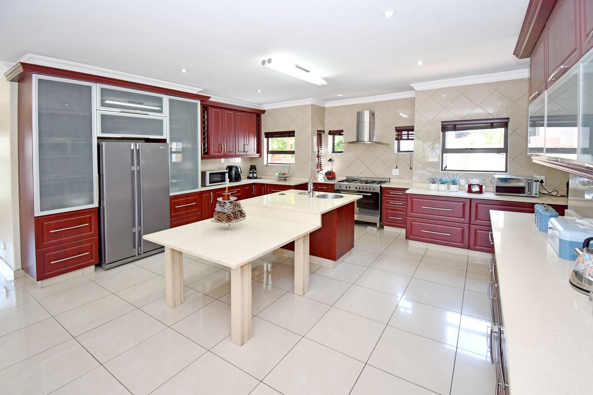 Spacious kitchen featuring dark wood cabinetry, stone countertops, a central island with integrated dining space, tiled flooring, and stainless steel appliances.