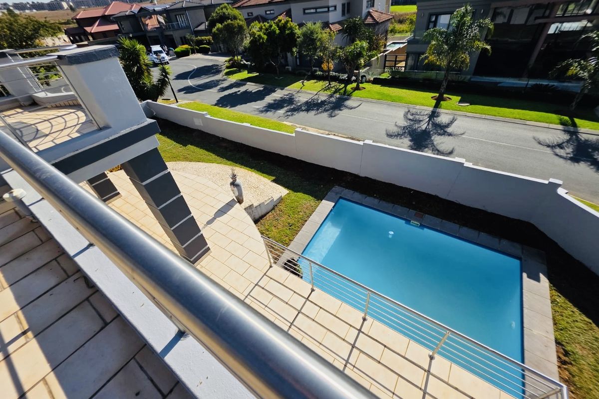 Elevated view from a balcony overlooking a private swimming pool, paved patio area, and the surrounding residential street.