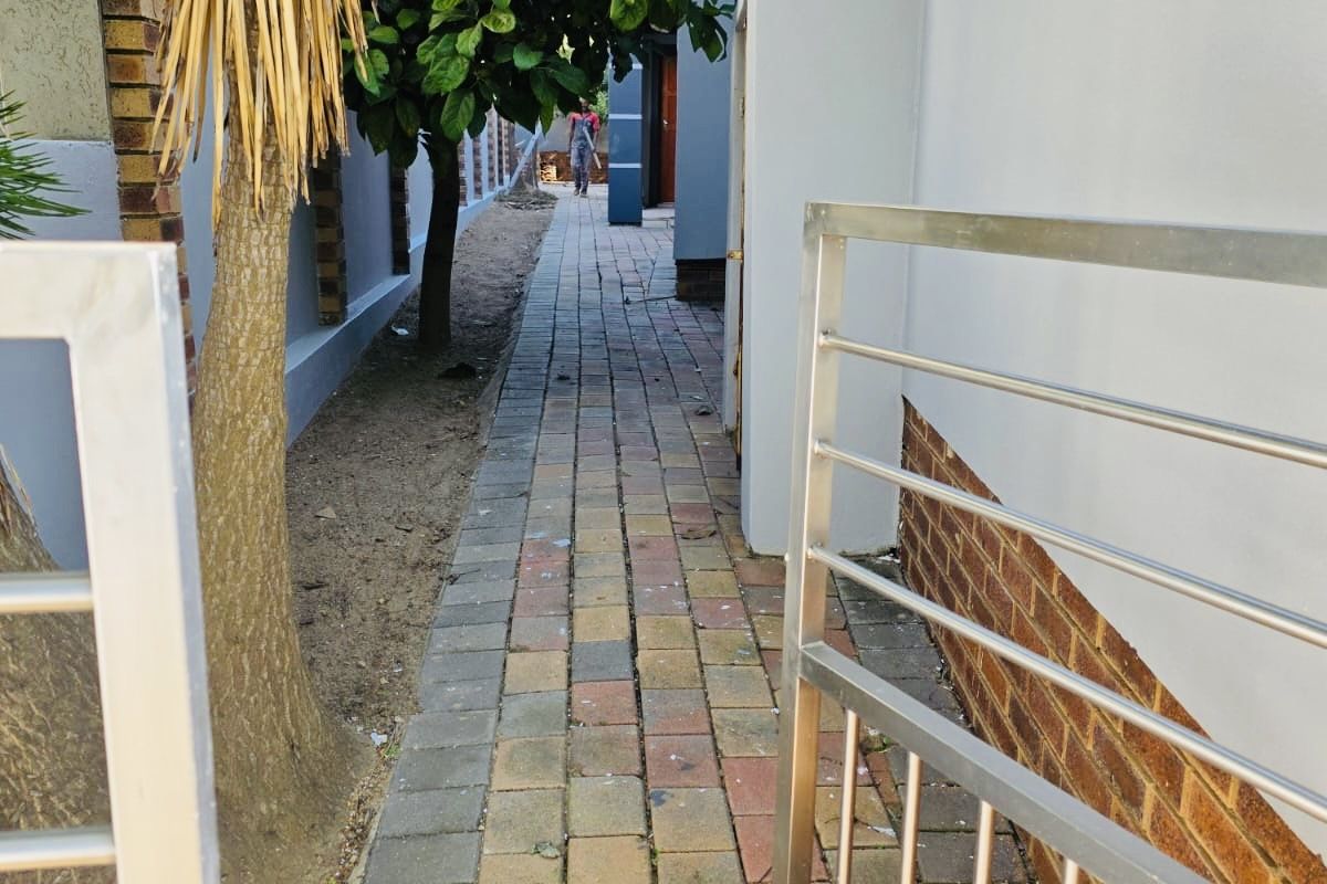 A side walkway featuring brick paving, stainless steel gate access, and perimeter walling along the side of the house.