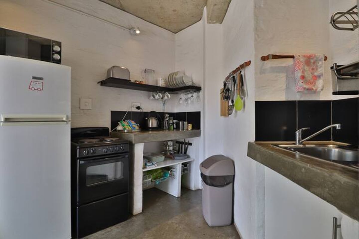 Compact kitchen featuring concrete countertops, stainless steel sink, electric stove, and exposed concrete ceiling with industrial-style finishes.