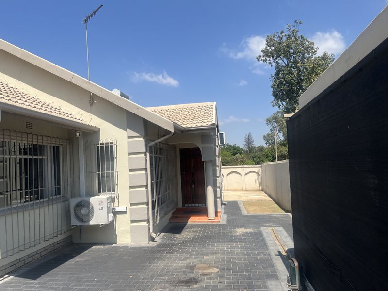 A view of the rear exterior of the house featuring paved flooring, security bars on windows, and an installed air conditioning unit.