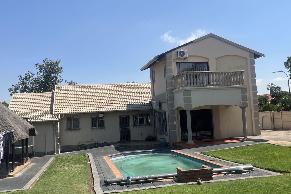 Rear view of a two-story house featuring a swimming pool, paved patio area, upper-level balcony, and a detached thatched lapa in the garden.