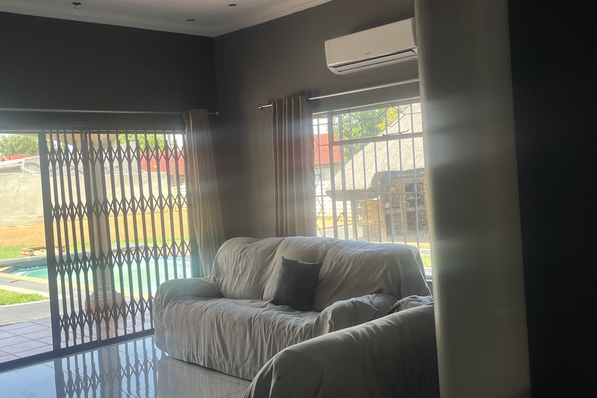 A living room featuring tiled flooring, a split-system air conditioner, and a sliding glass door with a security gate leading to the pool area.