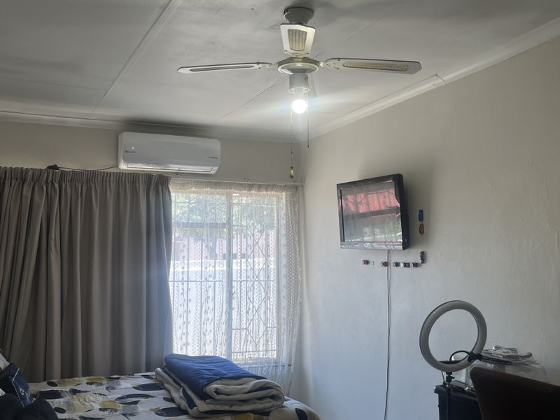 A bedroom featuring a ceiling fan, wall-mounted air conditioning unit, and security gate on the window.