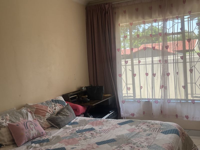 A bedroom featuring a window with security bars and curtain tracks, providing natural light and a view of the exterior.