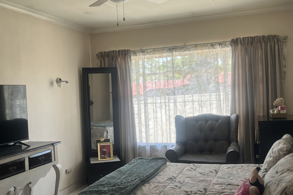 A bedroom featuring a ceiling fan, wall sconce lighting, and security bars on the window. The space shows minor signs of wear on the walls.