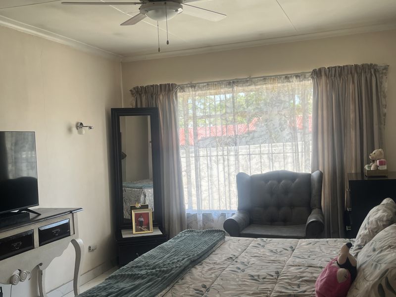 A bedroom featuring a ceiling fan, wall sconce lighting, and security bars on the window. The space shows minor signs of wear on the walls.