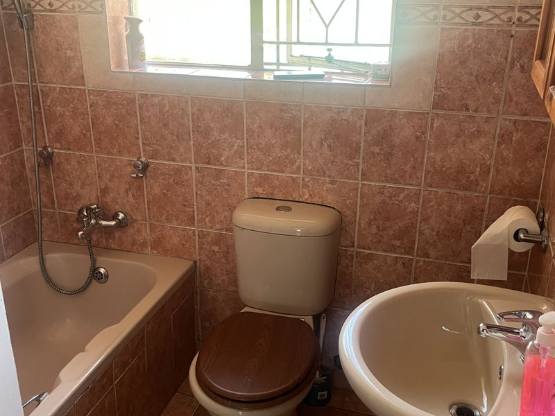 A functional bathroom featuring a bathtub, pedestal basin, and toilet with dated wall tiling and a window with security bars.