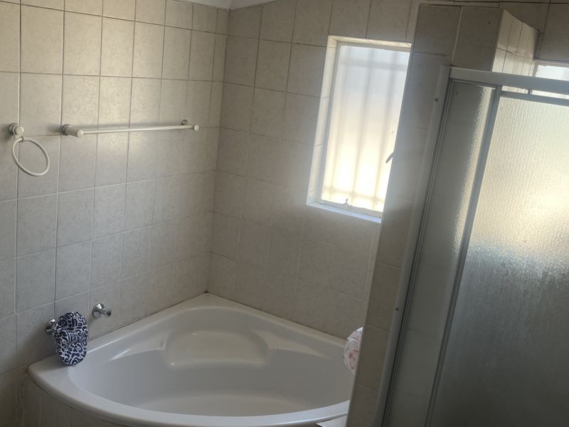 A functional bathroom featuring a corner bathtub, a separate shower enclosure, and neutral wall tiling with a frosted window for natural light.