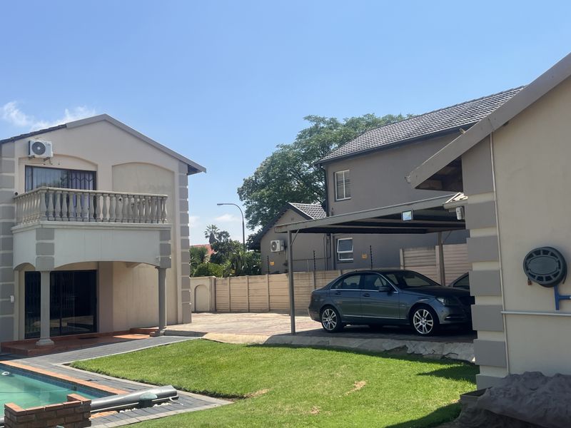 Rear exterior view featuring a swimming pool, paved driveway, carport, and a two-story building with a balcony.