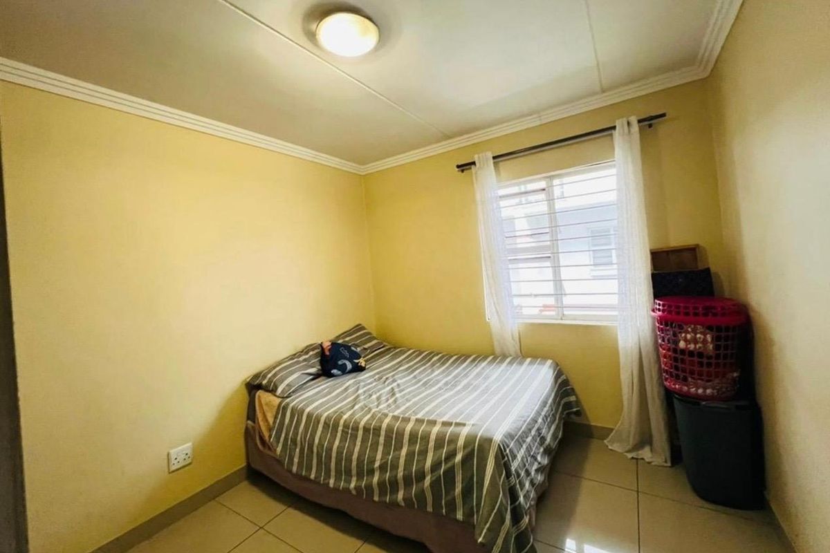 A standard bedroom featuring tiled flooring, a window with security bars, and a simple ceiling light fixture.
