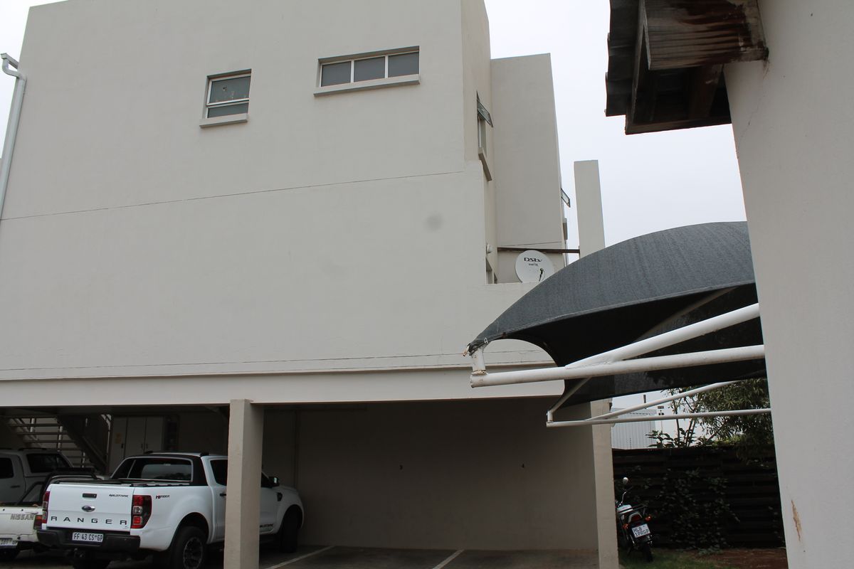 Rear view of the townhouse featuring a covered parking area with concrete pillars and an installed satellite dish.