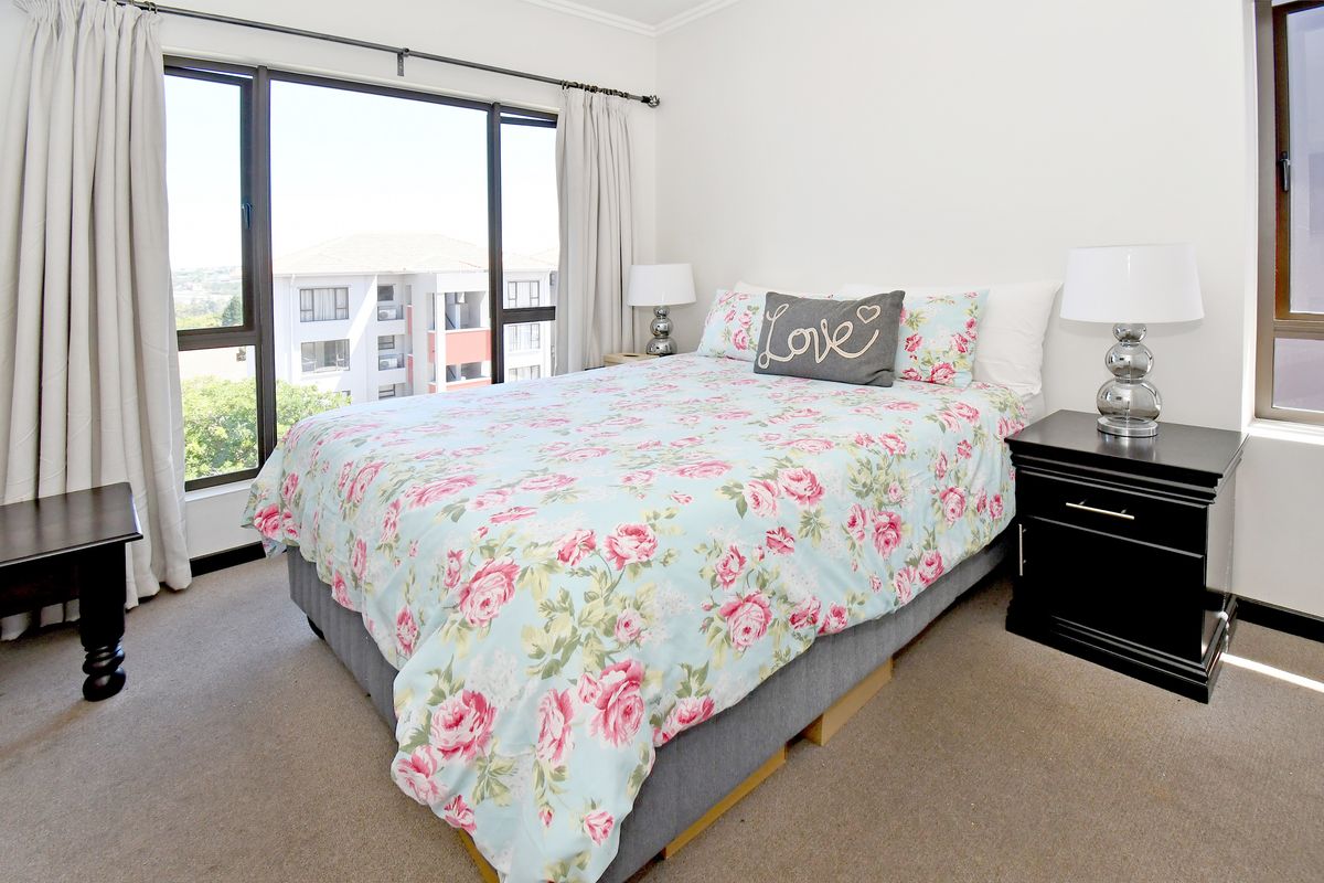 A bright bedroom featuring large windows with natural light, neutral wall finishes, and carpeted flooring.