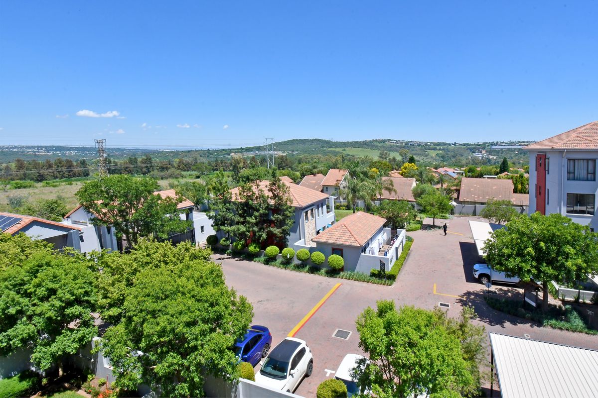 An elevated aerial view of the apartment complex grounds, featuring paved driveways, covered parking areas, and established landscaped gardens.