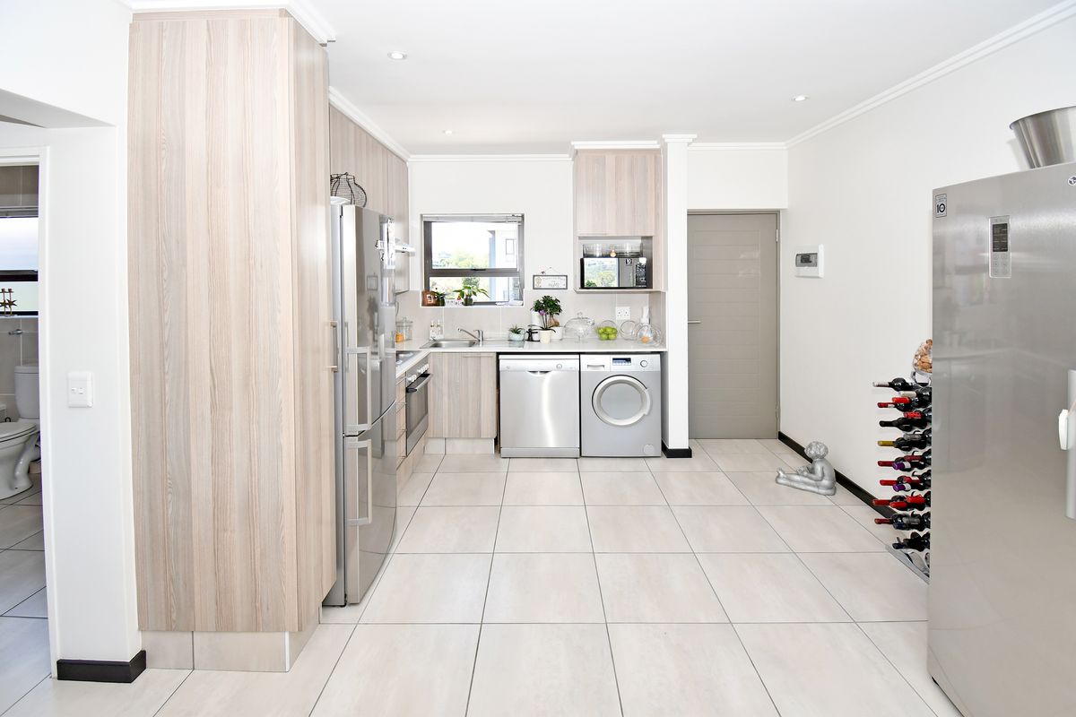Modern kitchen featuring light wood-grain cabinetry, tiled flooring, integrated appliances, and a functional layout with ample storage and counter space.