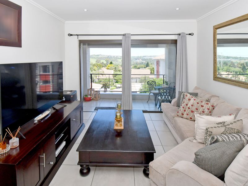 A bright living room featuring tiled flooring, recessed downlights, and a sliding glass door providing direct access to a balcony with scenic views.