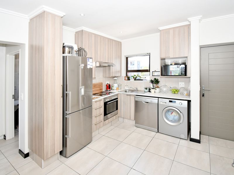 Modern kitchen featuring light wood-grain cabinetry, stainless steel appliances, tiled flooring, and integrated storage solutions in a clean, functional layout.