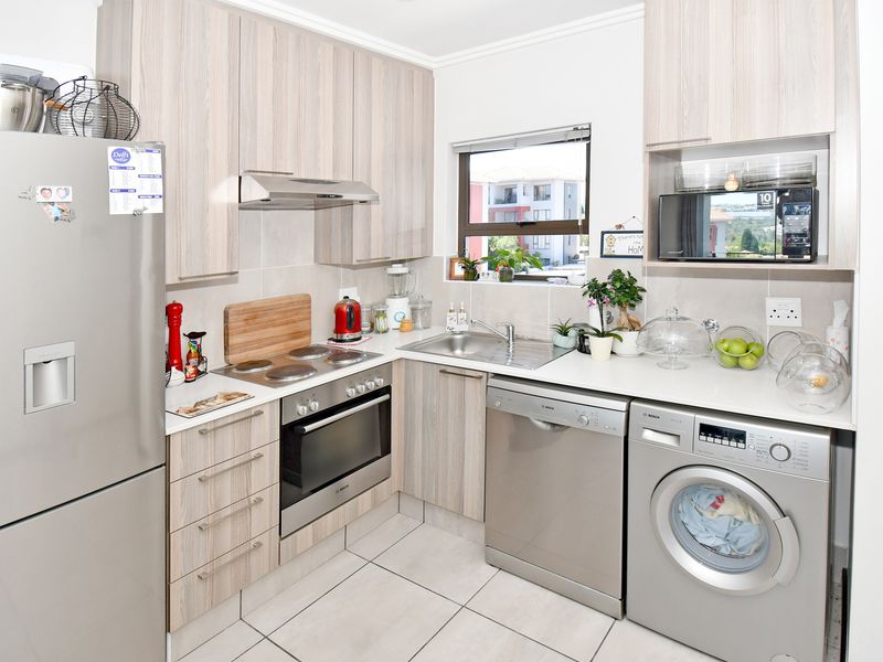 Modern kitchen featuring light wood-grain cabinetry, stainless steel appliances, tiled flooring, and a functional layout with integrated laundry and dishwasher space.