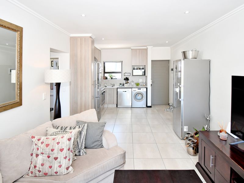 A bright open-plan living and kitchen area featuring modern cabinetry, tiled flooring, and recessed lighting, creating a functional and cohesive living space.