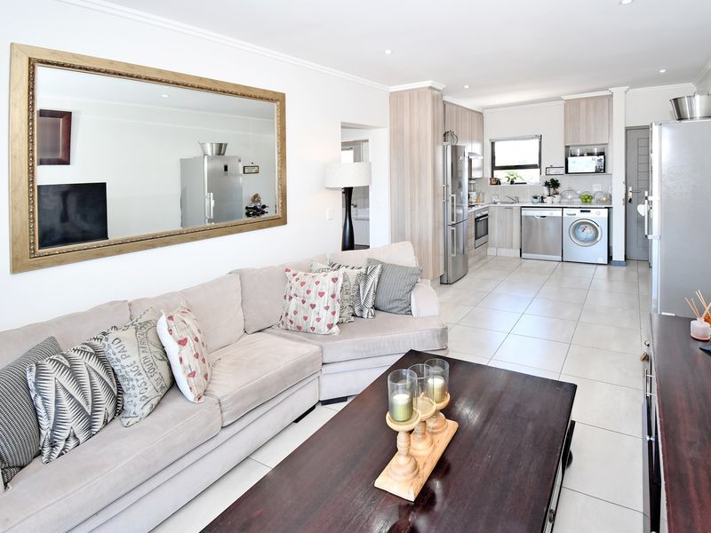 An open-plan living area featuring a modern kitchen with built-in cabinetry, tiled floors, and recessed lighting, seamlessly flowing into the lounge space.