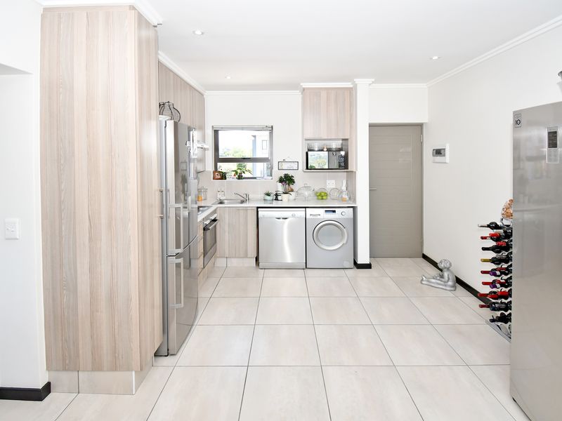 Modern kitchen featuring light wood-grain cabinetry, tiled flooring, integrated appliances, and a functional layout with ample storage and counter space.
