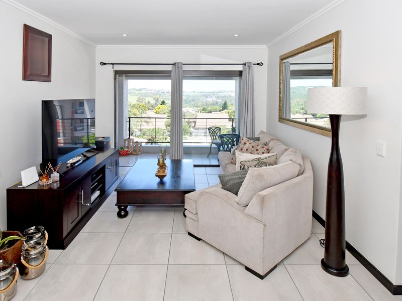A bright living room featuring neutral tiled flooring, recessed lighting, and a large sliding glass door providing access to a balcony with scenic views.