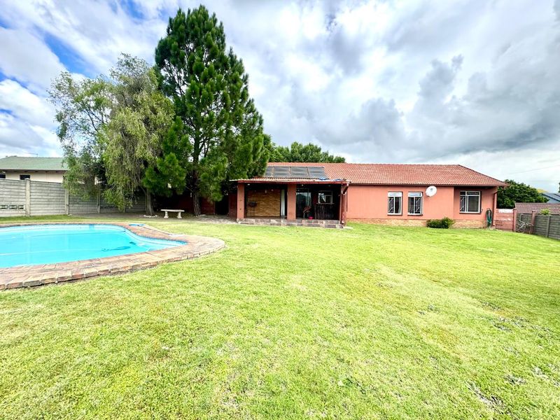 Rear view of the property featuring a swimming pool, a covered patio area, and a spacious lawn with established trees.