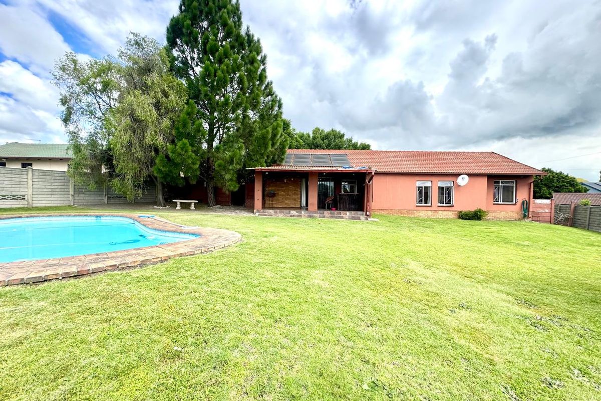 Rear view of the property featuring a swimming pool, a covered patio area, and a spacious lawn with established trees.