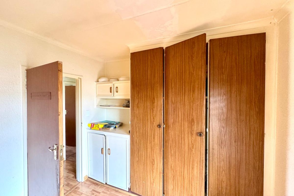 Bedroom featuring built-in wooden cupboards, laminate flooring, and built-in shelving, requiring some cosmetic attention to the ceiling and finishes.