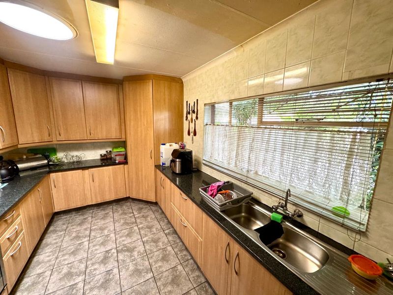 A functional kitchen featuring laminate cabinetry, granite countertops, a double stainless steel sink, and tiled splashbacks, offering a practical layout for daily use.
