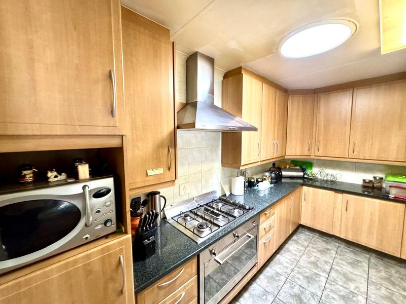 A functional kitchen featuring light wood-finish cabinetry, granite countertops, a gas hob with extractor fan, and tiled flooring, illuminated by a ceiling skylight.