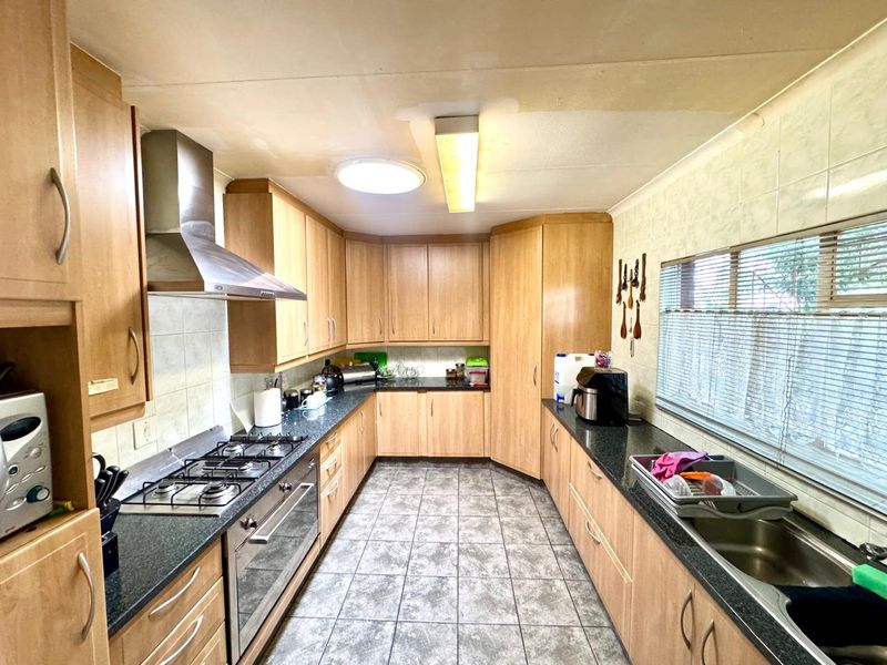 A functional kitchen featuring laminate cabinetry, granite countertops, a gas hob, built-in oven, and tiled flooring, offering a practical layout for daily meal preparation.