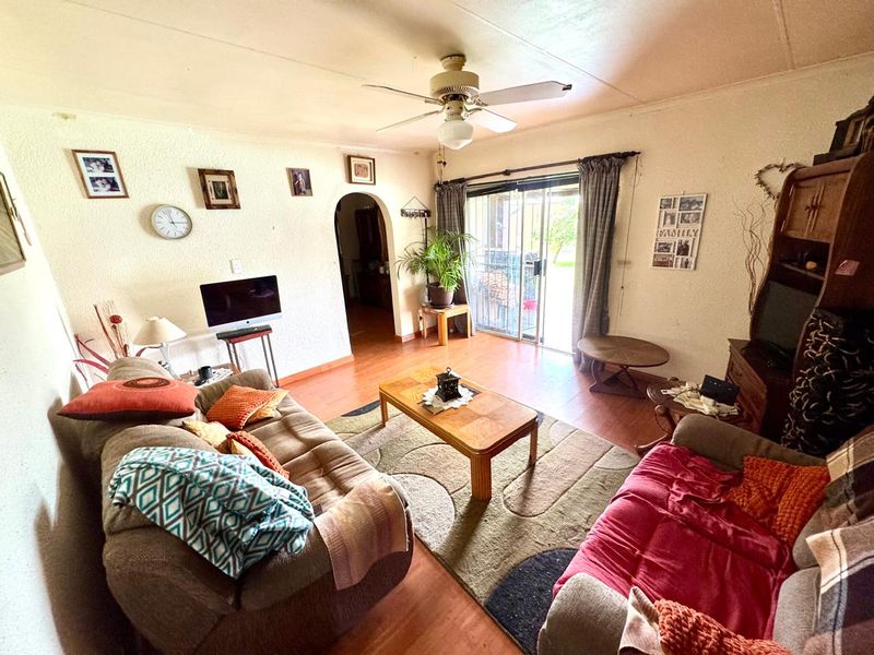 A living room featuring laminate flooring, a ceiling fan, and a sliding glass door providing access to the outdoor area.
