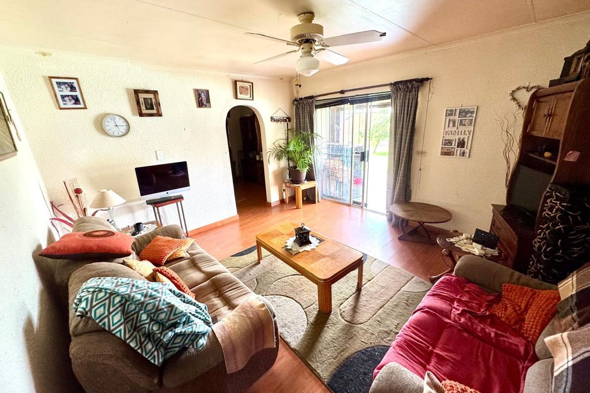 A living room featuring laminate flooring, a ceiling fan, and a sliding glass door providing access to the outdoor area.