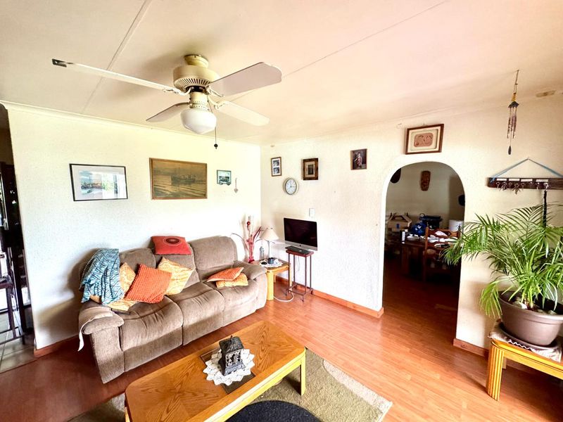 A living room featuring laminate flooring, a ceiling fan, and an arched doorway leading to an adjacent space.
