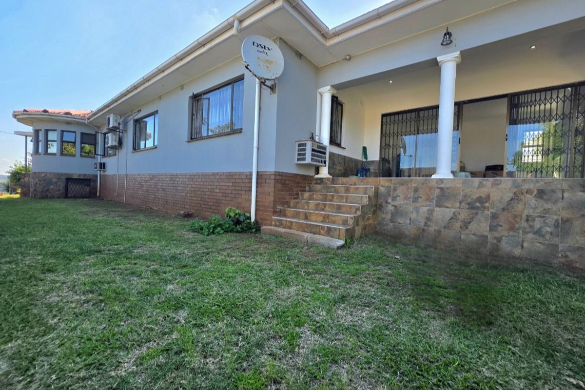 Rear exterior view of the house featuring a tiled patio, stone-clad base, security gates, and a lawn area.