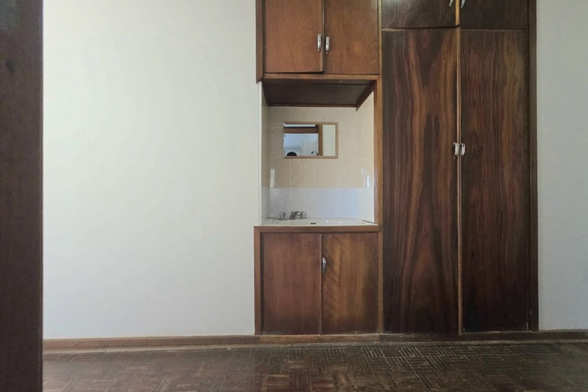 A bedroom featuring original parquet flooring, built-in wooden wardrobes, and a convenient integrated vanity basin area with tiled splashback.