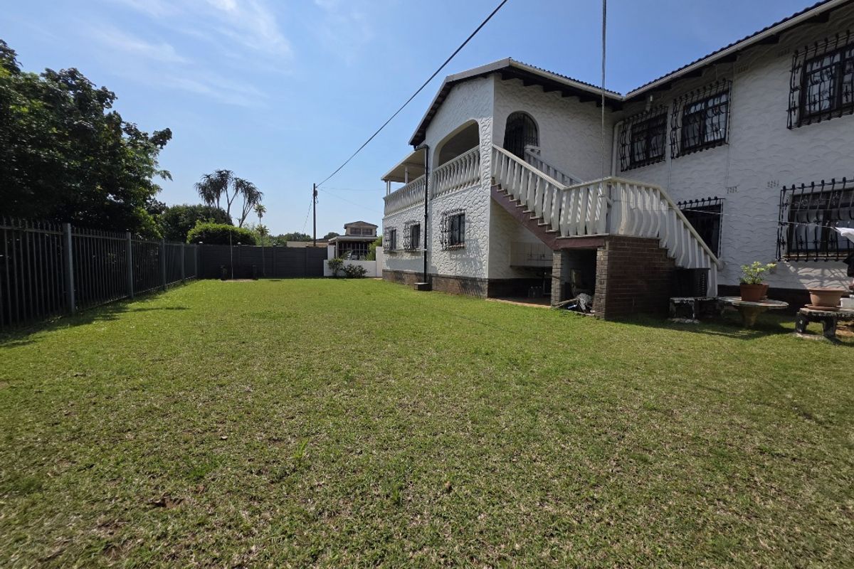Spacious rear garden featuring a large lawn, perimeter fencing, and an elevated balcony with an external staircase leading to the upper level.